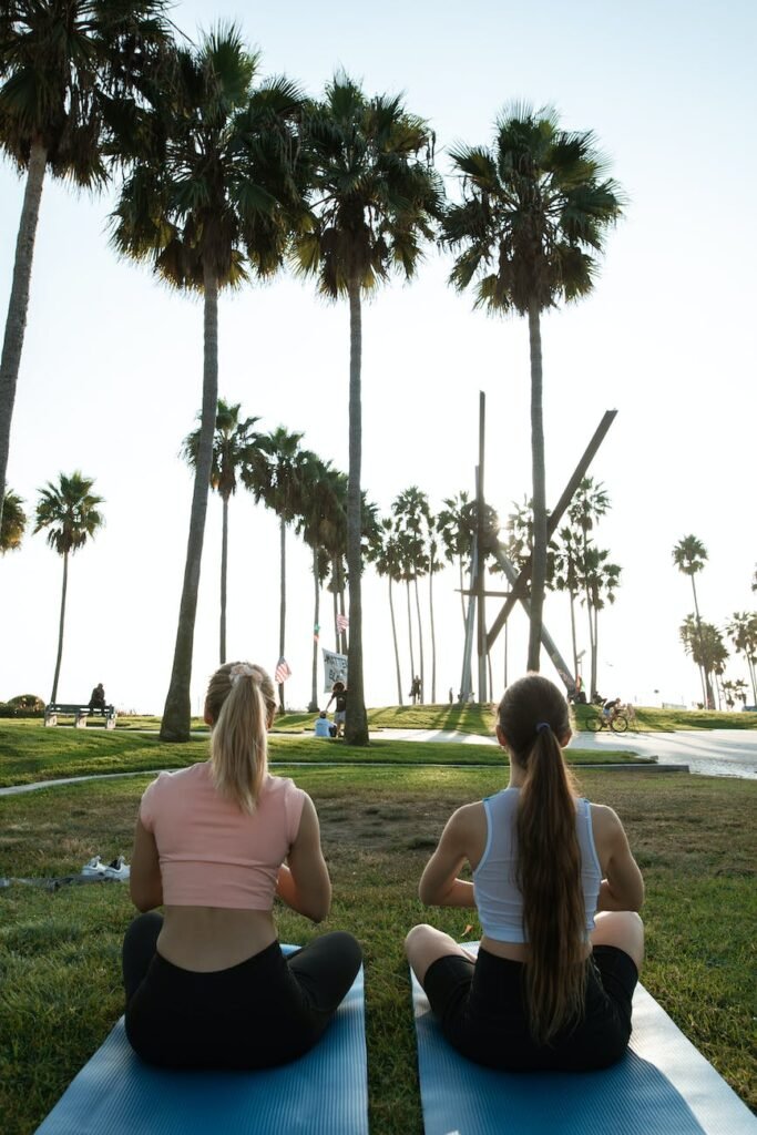 a pair of women sitting on yoga mats on grass