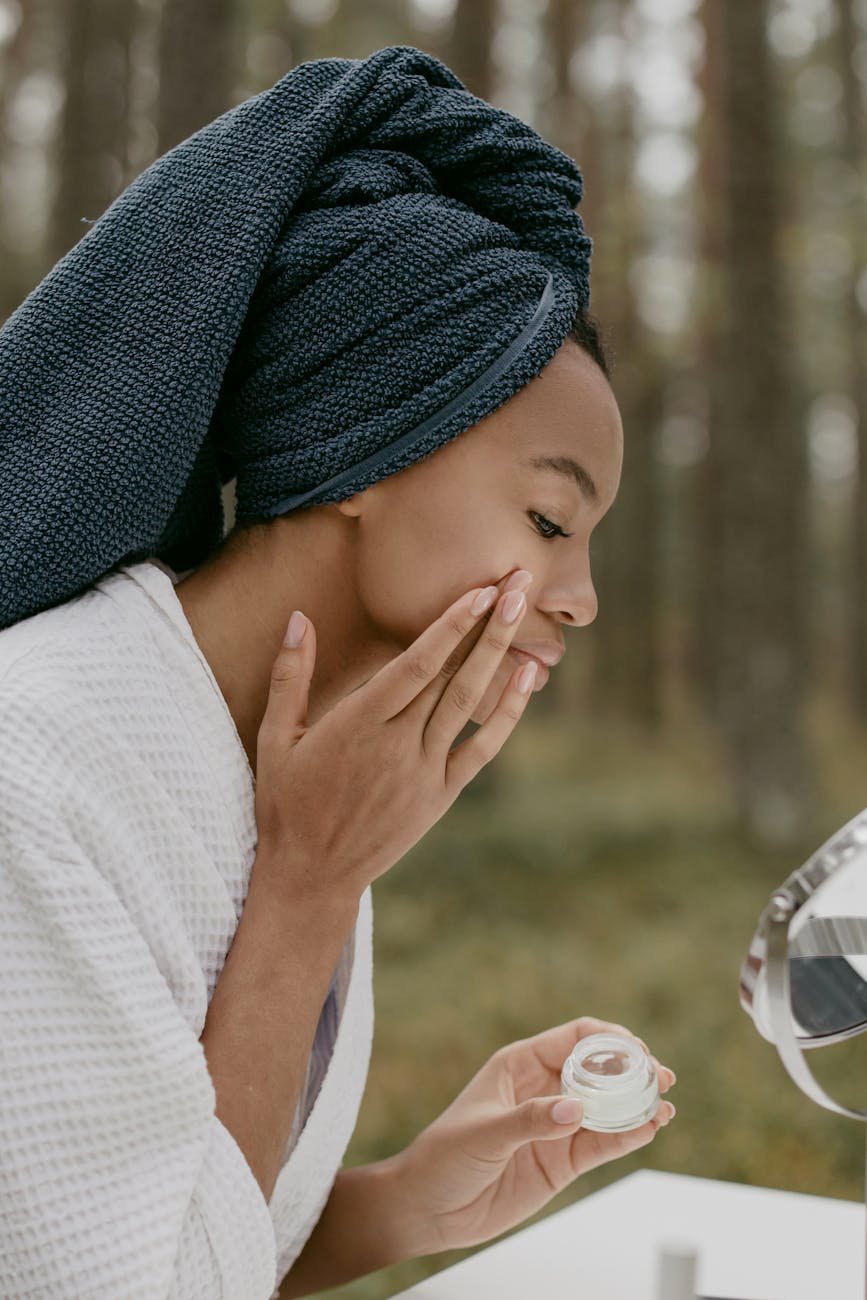 woman in white robe applying beauty product on her face